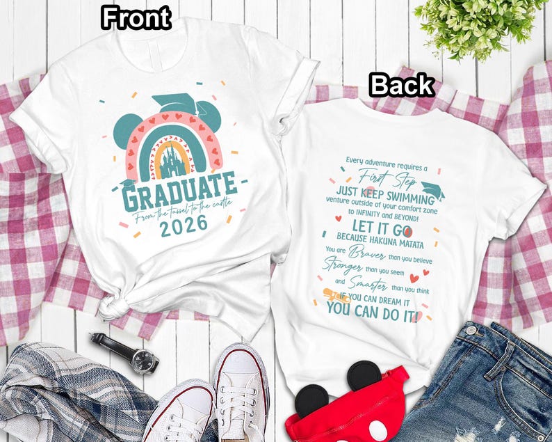 a white t-shirt with a colorful graphic and text, laid out on a wooden surface with a plaid blanket and a pair of sneakers.