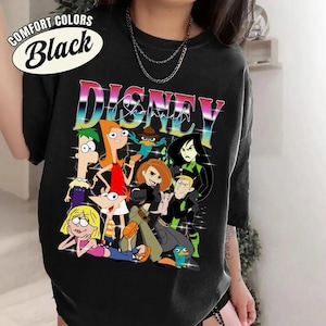 May include: Black t-shirt featuring a colorful graphic of Disney cartoon characters. The word "DISNEY" is displayed in a rainbow gradient font. The shirt also has the text "COMFORT COLORS Black" in a white oval.