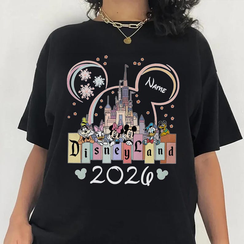 A black t-shirt with a Disney Land theme, featuring a castle, Minnie Mouse, Mickey Mouse, Donald Duck, and other Disney characters. The text "Disneyland" is displayed prominently, and the year "2026" is shown below.