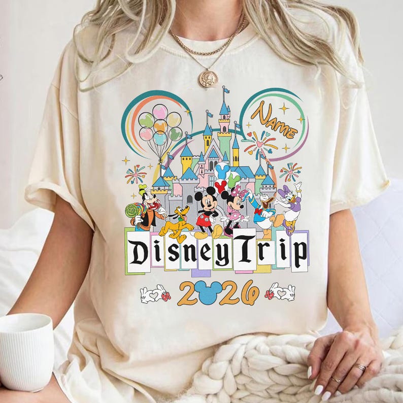 A person wearing a white t-shirt with a Disney-themed graphic design, including Mickey Mouse, Minnie Mouse, Donald Duck, and other Disney characters, along with a castle and fireworks. The text on the t-shirt says "Disney Trip" and "20".