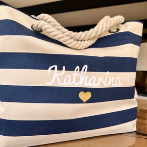 May include: A white and navy blue striped tote bag with a rope handle. The bag has the name "Katharina" embroidered in white with a gold heart below it.