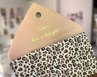 Puede incluir: Un bolso de mano beige con un estampado de leopardo en el exterior. La solapa interior es de color beige liso con el texto "Schön, dass es dich gibt!" en escritura amarilla. El bolso de mano está abierto, revelando el interior.