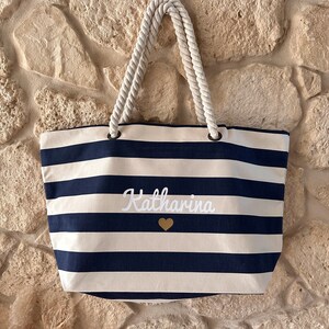 May include: A white and navy blue striped tote bag with rope handles. The bag has the name "Katharina" embroidered on the front in white with a gold heart.