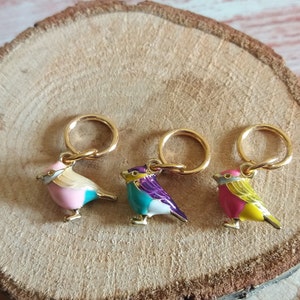 May include: Three gold stitch markers with colorful bird charms. The birds are pink and teal, teal and purple, and pink and yellow.