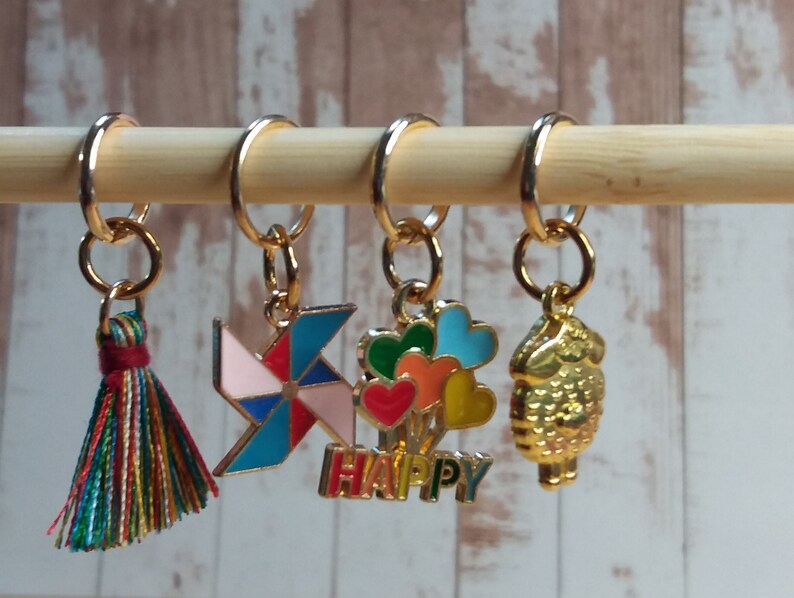 Pu&ograve; includere: Cinque marcapunti colorati con diversi design. I marcapunti sono attaccati a un bastoncino di legno. I design includono un fiocco, una girandola, un mazzo di palloncini con la scritta "HAPPY" sotto e un uccello dorato.