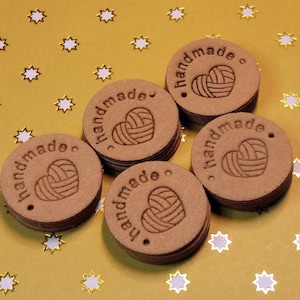 May include: Six brown round tags with the word "handmade" and a heart with yarn inside. The tags are on a gold background with white stars.