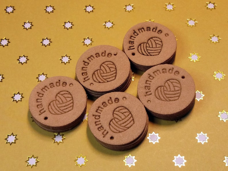 May include: Six brown round tags with the word "handmade" and a heart with yarn inside. The tags are on a gold background with white stars.