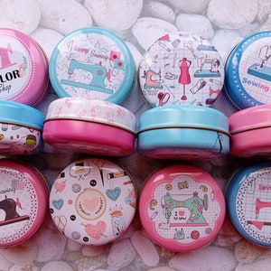 Op de afbeelding: Een verzameling ronde, decoratieve blikken dozen met deksels, met naaipatronen. De blikken zijn in verschillende kleuren, waaronder roze en blauw, en tonen afbeeldingen van naaimachines, garenklosjes en de tekst "Tailor Shop" en "Sewing Time".