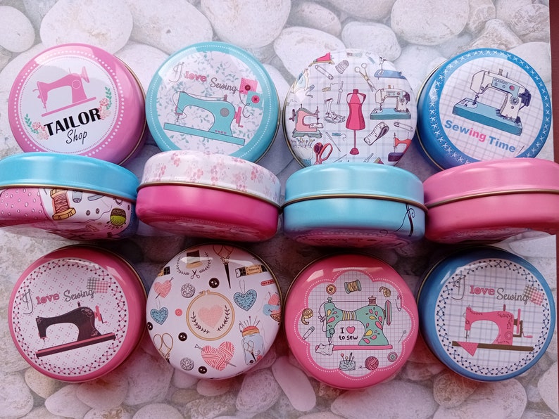 Op de afbeelding: Een verzameling ronde, decoratieve blikken dozen met deksels, met naaipatronen. De blikken zijn in verschillende kleuren, waaronder roze en blauw, en tonen afbeeldingen van naaimachines, garenklosjes en de tekst "Tailor Shop" en "Sewing Time".