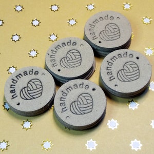 May include: Five brown round paper tags with the word "handmade" and a heart-shaped yarn ball design. The tags are on a gold background with white stars.