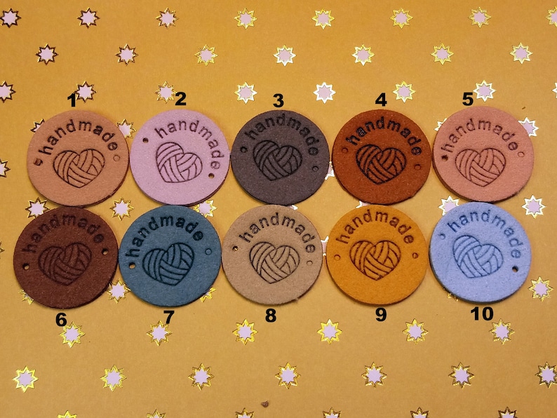 May include: Ten round leather tags with the word "handmade" and a heart design in various colours, including brown, pink, blue, and tan.