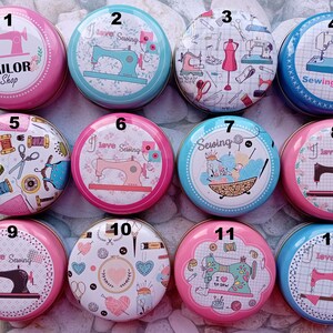 Op de afbeelding: Een verzameling van twaalf ronde, decoratieve blikken met naaigerelateerde ontwerpen. De blikken tonen afbeeldingen van naaimachines, garen, scharen en de tekst "Tailor Shop", "I love Sewing" en "Sewing Time". De blikken zijn in verschillende kleuren, waaronder roze, blauw en wit.