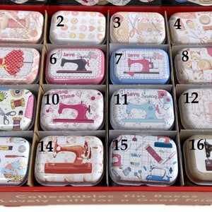 Peut inclure: Un ensemble de 16 petites boîtes en étain rectangulaires avec différents motifs sur le thème de la couture. Les boîtes sont disposées en grille et numérotées de 1 à 16. Certains des motifs comprennent des machines à coudre, des bobines de fil, des ciseaux et les mots "J'aime la couture".