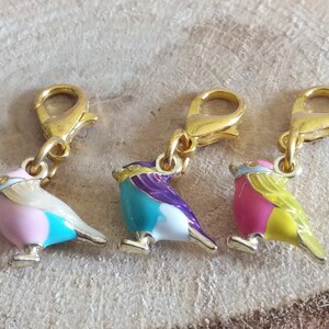 May include: Three gold-tone bird charms with enamel paint in pink, blue, and yellow. Each charm has a gold-tone lobster clasp.