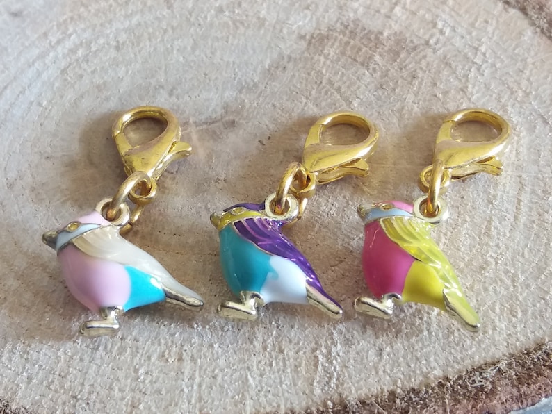 May include: Three gold-tone bird charms with enamel paint in pink, blue, and yellow. Each charm has a gold-tone lobster clasp.