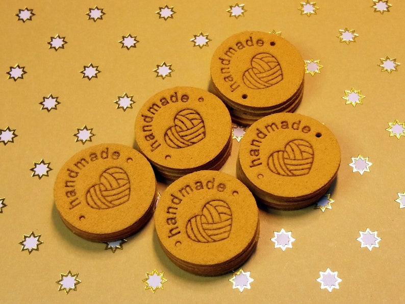 May include: Six round, brown, wooden tags with the word "handmade" and a heart-shaped yarn ball design. The tags are on a gold background with white stars.