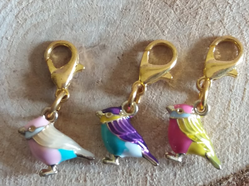 May include: Three gold bird charms with enamel paint. The birds are pink and yellow, blue and purple, and white and pink.