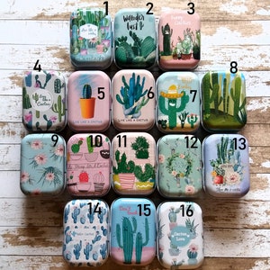 Peut inclure: Une collection de seize boîtes métalliques rectangulaires, chacune avec un design unique sur le thème des cactus. Les boîtes présentent diverses couleurs, dont le vert, le bleu, le rose et le blanc, avec des textes tels que "Live Like a Cactus" et "Cactus Love".