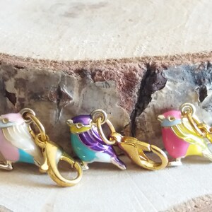 May include: Four colorful enamel bird charms with gold-tone clasps. The birds are pink and blue, purple and turquoise, turquoise and white, and pink and yellow.