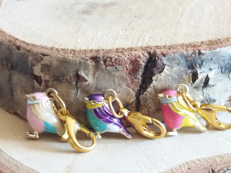 May include: Four colorful enamel bird charms with gold-tone clasps. The birds are pink and blue, purple and turquoise, turquoise and white, and pink and yellow.