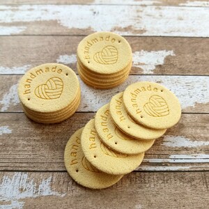 May include: A stack of 10 yellow round leather tags with the words "handmade" and a heart with yarn inside.