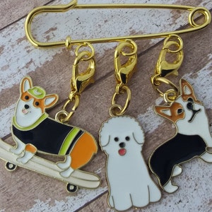 Peut inclure: Épingle de sûreté dorée avec trois breloques sur le thème des chiens. Une breloque corgi sur un skateboard, un Bichon Frise blanc et un autre corgi. Les breloques ont des fermoirs dorés.