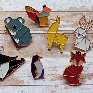 Peut inclure: Ensemble de dix épingles en forme d'animaux origami, comprenant un koala, un panda, un renard, un pingouin, un lapin, un écureuil et un lama. Les épingles sont en métal et ont une finition dorée.