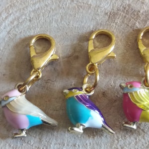 May include: Three gold-tone bird charms with colorful enamel paint. Each charm features a different color combination of pink, blue, yellow, white, and purple. The charms have a lobster claw clasp.