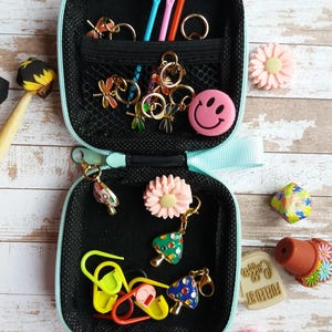 Puede incluir: Peque&ntilde;o estuche negro con cremallera y ribete azul claro, lleno de varios suministros para manualidades. Incluye marcadores de punto, abalorios y agujas de varios colores. Elementos decorativos: carita sonriente, flores y abalorios de setas. Accesorios de artesan&iacute;a.