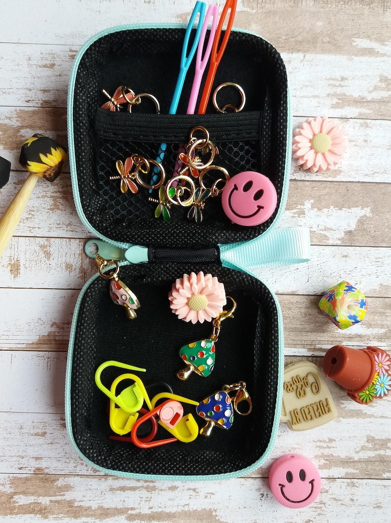 Puede incluir: Peque&ntilde;o estuche negro con cremallera y ribete azul claro, lleno de varios suministros para manualidades. Incluye marcadores de punto, abalorios y agujas de varios colores. Elementos decorativos: carita sonriente, flores y abalorios de setas. Accesorios de artesan&iacute;a.