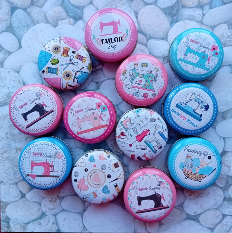 Op de afbeelding: Een verzameling ronde, decoratieve blikken met naaigerelateerde ontwerpen. De blikken tonen afbeeldingen van naaimachines, garenklosjes, scharen en de tekst "TAILOR Shop", "I love Sewing" en "Sewing Time". De blikken zijn in verschillende kleuren, waaronder roze, blauw en wit.