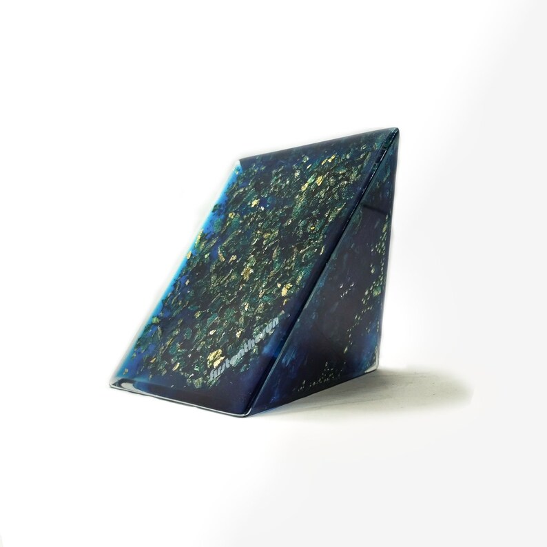 May include: A triangular, abstract art piece with a dark blue base, speckled with gold leaf. The artwork has a glossy finish and is set against a white background. The text "Juthentherin" is visible on the side.