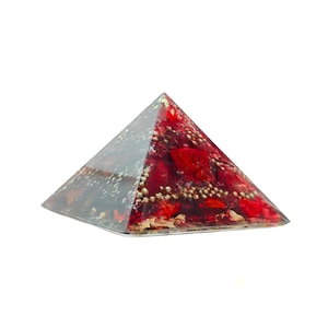 May include: A transparent pyramid with a red and gold interior, and small gold-colored spheres. The pyramid is set against a white background. The pyramid's sides are clear, allowing a view of the interior.