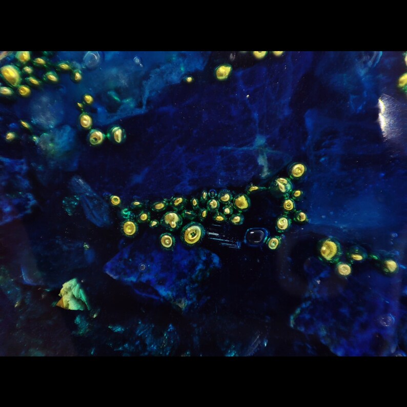 May include: Abstract art piece with a dark blue and teal background. The artwork features clusters of yellow and green circular shapes, creating a unique visual texture. The piece has a glossy finish, enhancing the depth and color variations.
