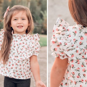 May include: A white blouse with a pink floral print and ruffled sleeves. The blouse has a high neck and a button closure in the front.