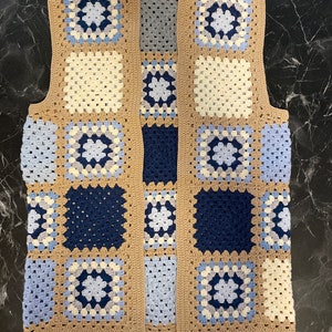 Könnte beinhalten: Eine gehäkelte Weste mit Patchwork-Muster aus Quadraten in Blautönen, Beige und Weiß.