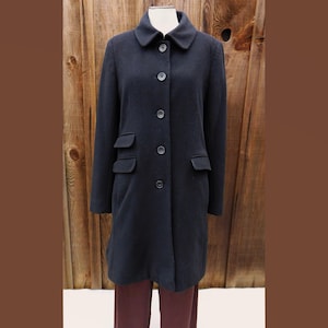 May include: A dark navy blue coat with a classic design. The coat features a collared neckline, button-down closure, and two front pockets. The coat is displayed on a mannequin against a wooden background.
