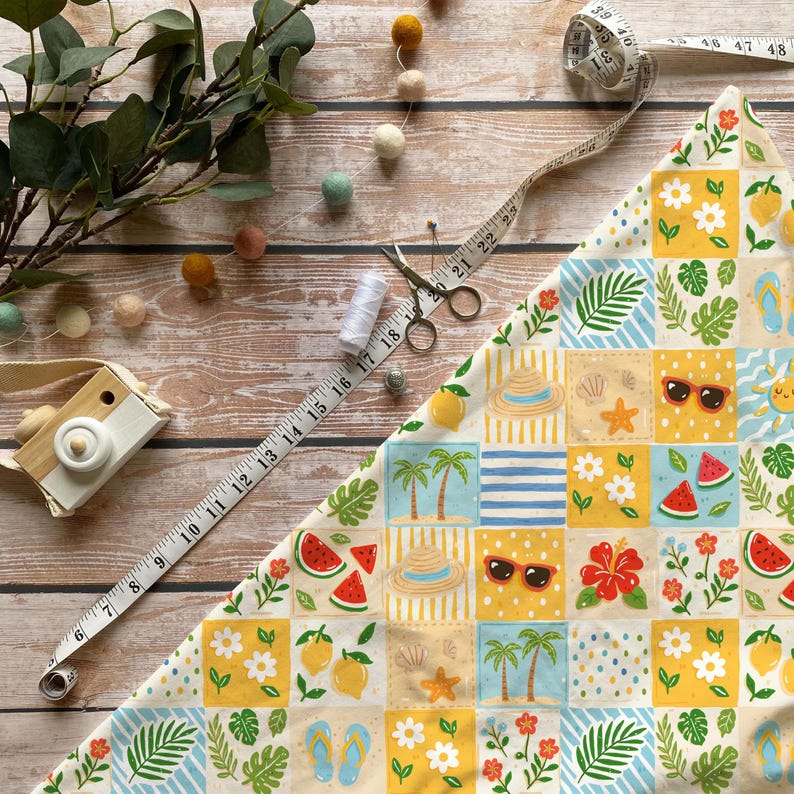 May include: A colorful summer-themed fabric with a patchwork design featuring sunglasses, palm trees, and watermelon slices. A measuring tape, scissors, thread, and a wooden toy camera are also present, suggesting crafting or sewing.