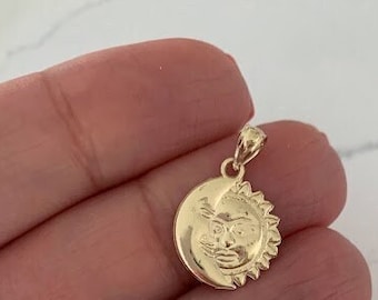 May include: A gold pendant featuring a sun and moon design. The sun has a face and the moon is a crescent shape.