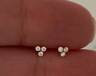 May include: A pair of small, silver earrings each featuring three tiny, clear diamonds.