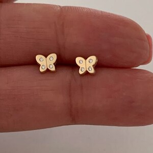 Könnte beinhalten: Ein Paar goldene Schmetterlings-Ohrringe mit kleinen, klaren Steinen.