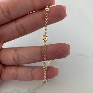 May include: A gold chain necklace with a delicate, mariner link design. The chain is shown on a hand, with the ends of the chain visible.