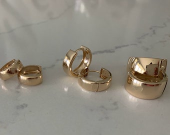 May include: Three pairs of gold hoop earrings of different sizes. The earrings are all made of a smooth, shiny metal.