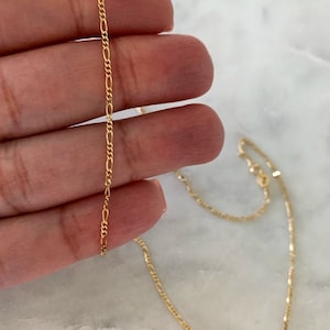 May include: A gold chain necklace with a delicate, thin, and flat design. The chain is made of a fine, smooth metal and has a simple, elegant look.