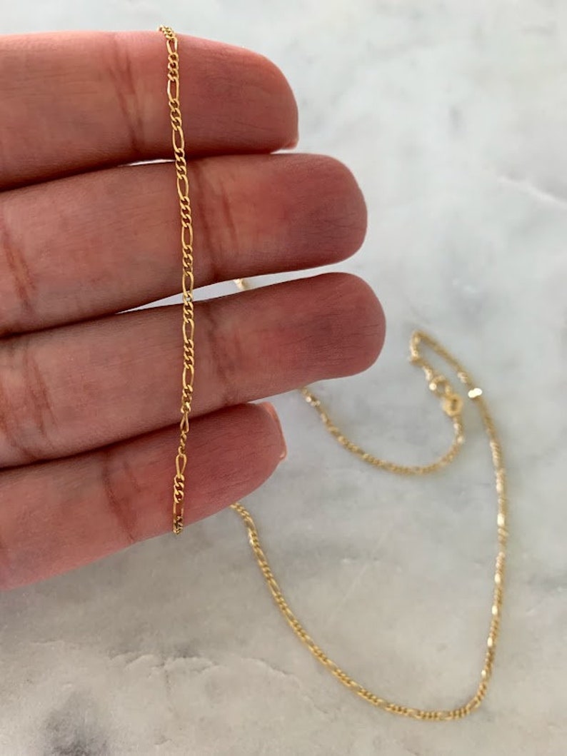 May include: A gold chain necklace with a delicate, thin, and flat design. The chain is made of a fine, smooth metal and has a simple, elegant look.