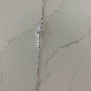 Puede incluir: Un brazalete de cadena de plata con un peque&ntilde;o dije con forma de cruz y coraz&oacute;n.