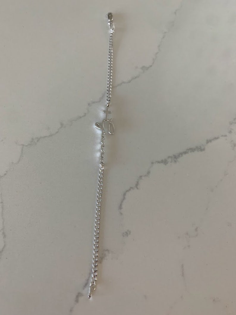 Puede incluir: Un brazalete de cadena de plata con un peque&ntilde;o dije con forma de cruz y coraz&oacute;n.