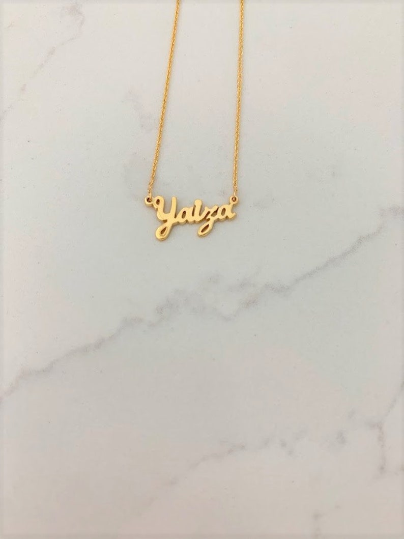 May include: A gold necklace with the name "Yalza" written in cursive.