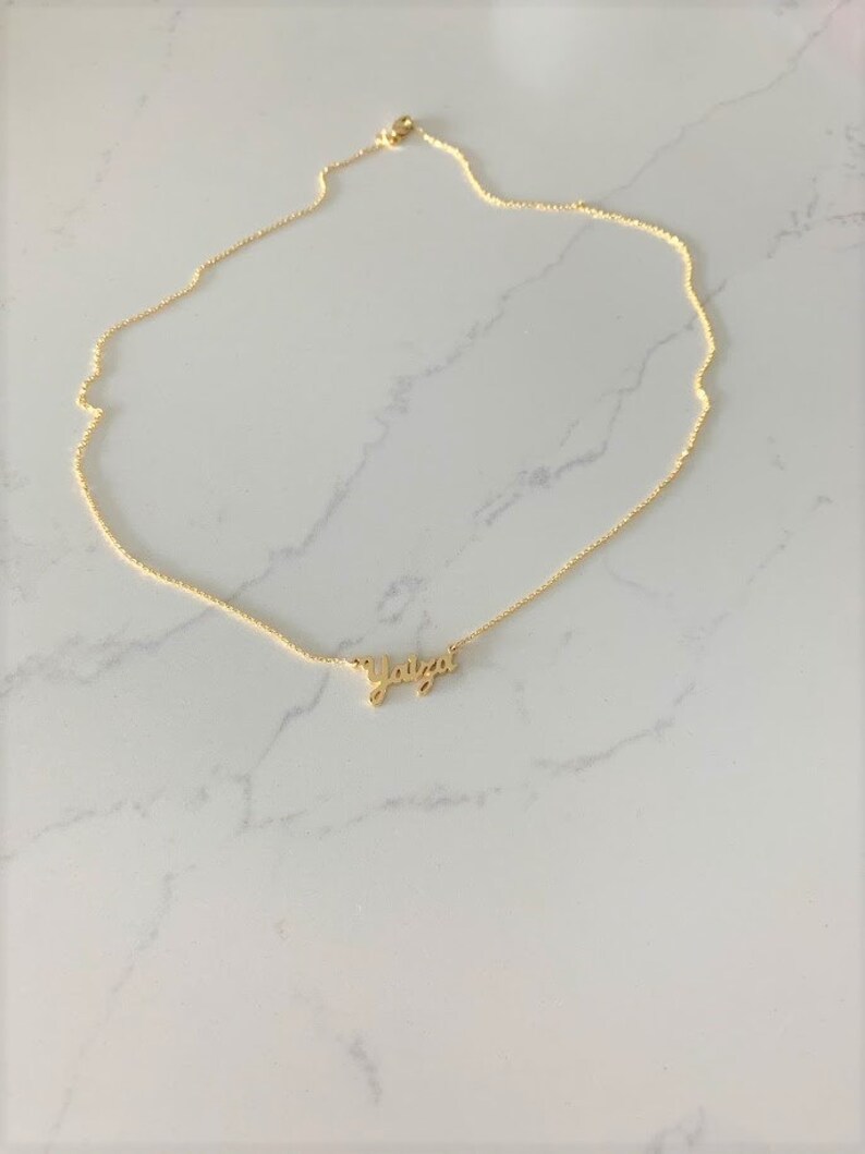 May include: A gold chain necklace with a delicate pendant that reads "Yaitza".