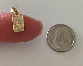 Könnte beinhalten: Ein goldfarbener Anhänger mit einem religiösen Bild einer Person mit Heiligenschein. Der Anhänger ist rechteckig und hat ein detailliertes Design. Der Anhänger wird neben einem US-Dime zur Größenvergleich gezeigt.